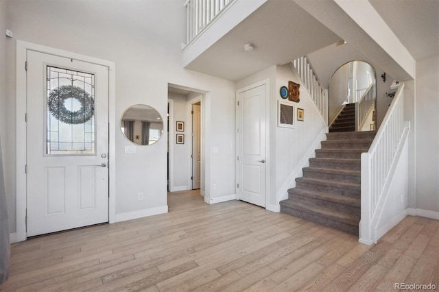 foyer entrance with baseboards, stairs, and light wood-style floors