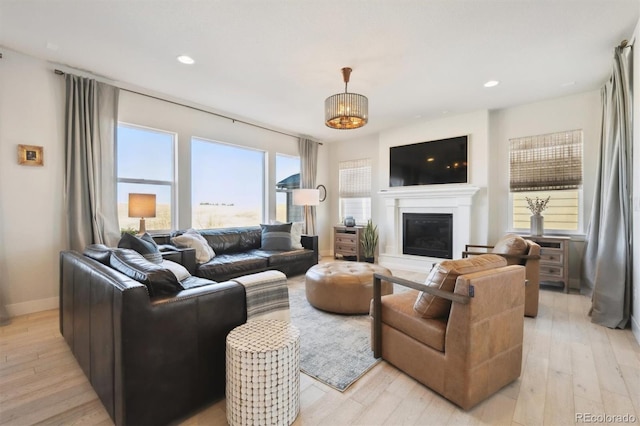 living area with recessed lighting, light wood-type flooring, a glass covered fireplace, and baseboards