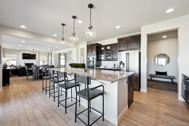 kitchen with dark brown cabinetry, stainless steel fridge with ice dispenser, light wood-style flooring, a breakfast bar, and a fireplace