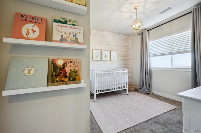 bedroom featuring wooden walls, visible vents, carpet, a nursery area, and a notable chandelier