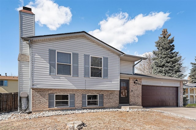 tri-level home with brick siding, a chimney, an attached garage, fence, and driveway