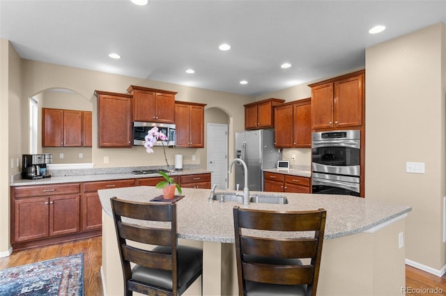 16685 E 101st Ave, Commerce City, CO 80022 - kitchen with a kitchen island with sink, light wood-style floors, arched walkways, a sink, and appliances with stainless steel finishes