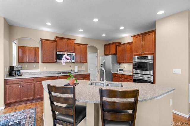 16685 E 101st Ave, Commerce City, CO 80022 - kitchen with a kitchen island with sink, light wood-style floors, arched walkways, a sink, and appliances with stainless steel finishes