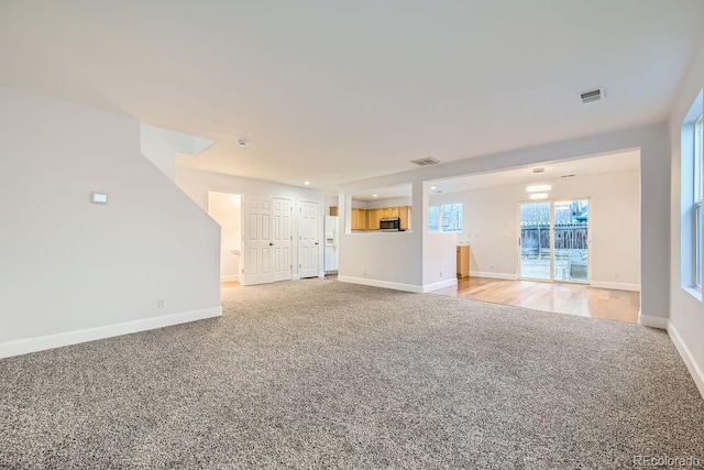 unfurnished living room featuring baseboards, visible vents, and light colored carpet