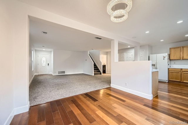 unfurnished living room with baseboards, visible vents, dark wood finished floors, stairway, and a notable chandelier