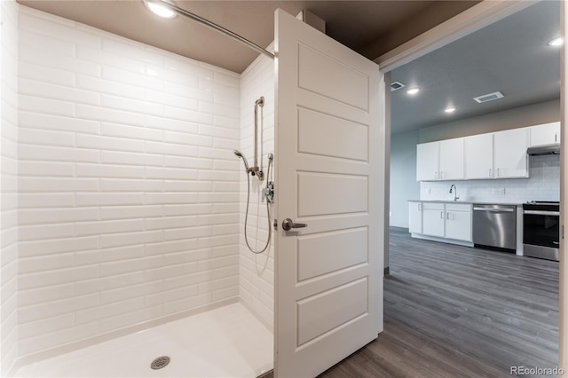 bathroom with wood-type flooring, vanity, a tile shower, and tasteful backsplash