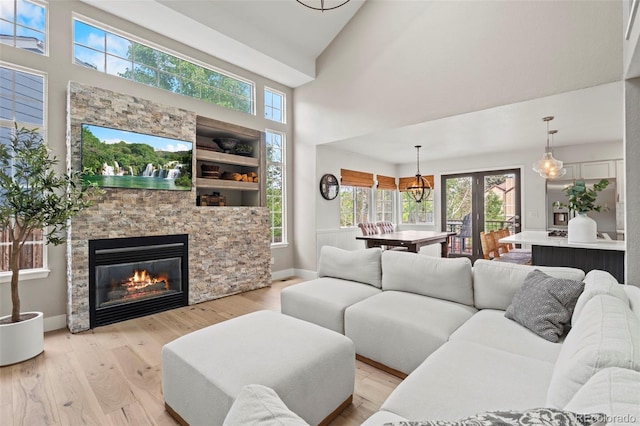 9432 La Quinta Way, Lone Tree, CO 80124 - living room featuring light wood-type flooring, a stone fireplace, healthy amount of natural light, a towering ceiling, and a chandelier