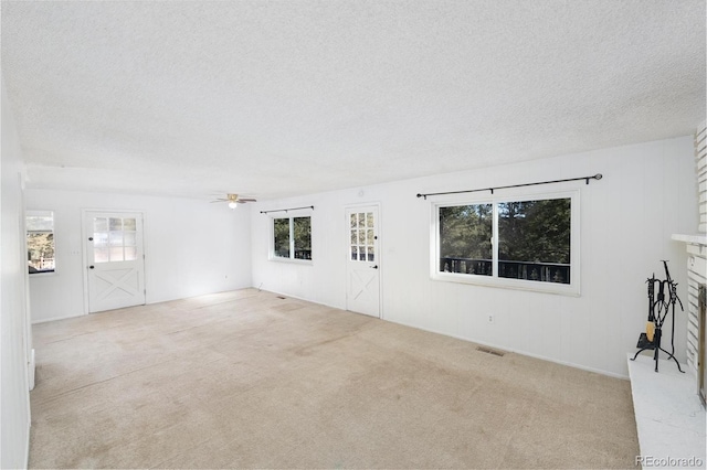 unfurnished living room with ceiling fan, light carpet, a textured ceiling, and a brick fireplace