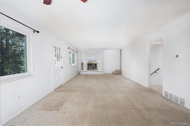 unfurnished living room featuring ceiling fan, a fireplace, light colored carpet, and a textured ceiling