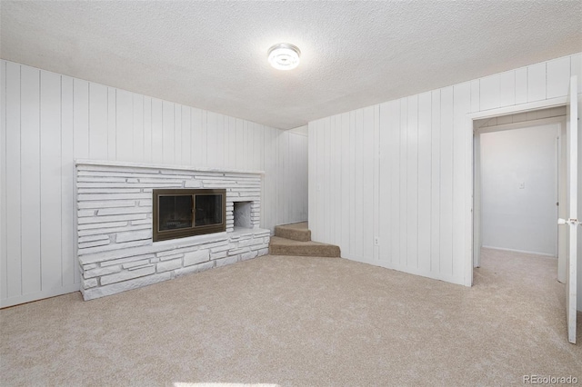 unfurnished living room with a textured ceiling, light colored carpet, and a stone fireplace