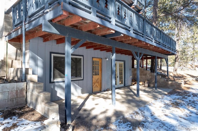 snow covered back of property featuring french doors, a patio area, and a wooden deck