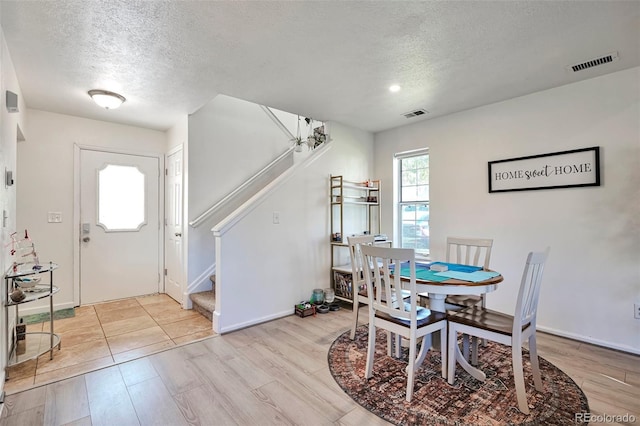 dining space featuring a textured ceiling, stairs, light wood-style floors, and baseboards