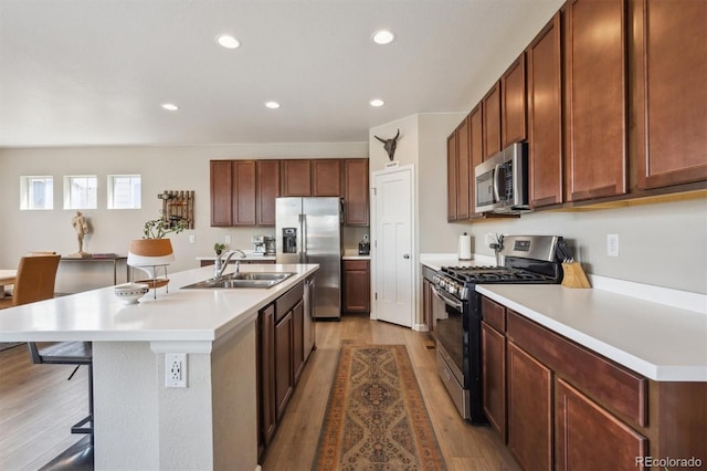 kitchen with appliances with stainless steel finishes, a breakfast bar, a sink, and light wood-type flooring