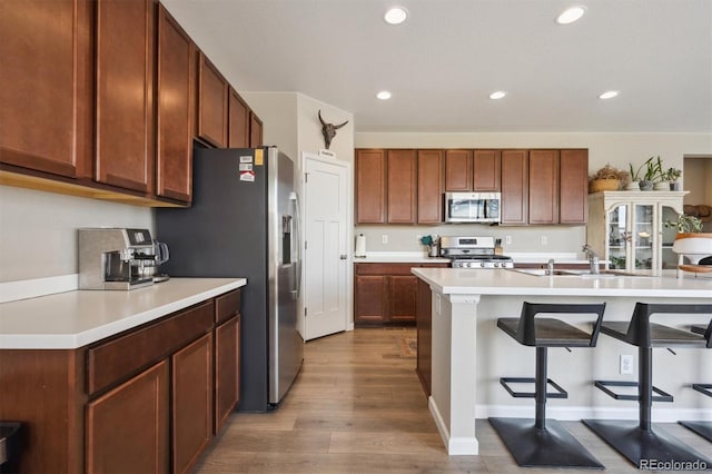 kitchen with a kitchen breakfast bar, appliances with stainless steel finishes, wood finished floors, a sink, and recessed lighting