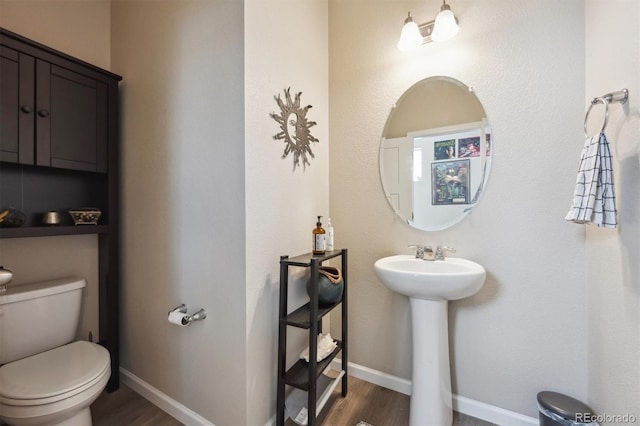 half bathroom featuring baseboards, a sink, wood finished floors, and toilet