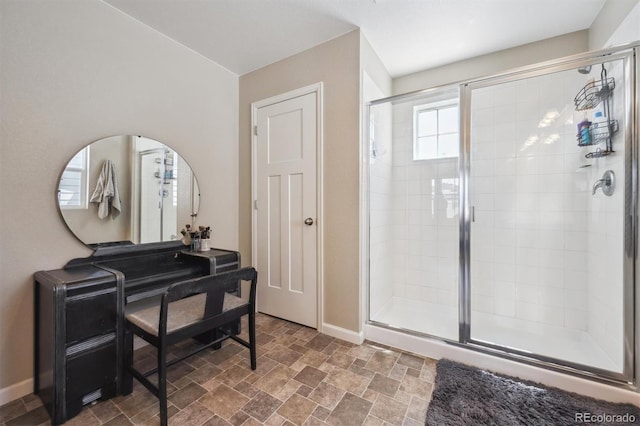 full bath with baseboards, stone finish flooring, and a stall shower