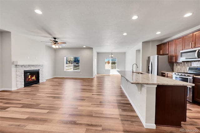 kitchen with sink, a stone fireplace, an island with sink, decorative backsplash, and appliances with stainless steel finishes