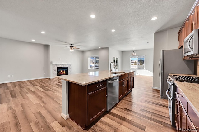 kitchen featuring sink, hanging light fixtures, an island with sink, a textured ceiling, and appliances with stainless steel finishes