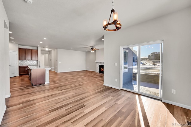 unfurnished living room featuring ceiling fan with notable chandelier, light hardwood / wood-style floors, and sink