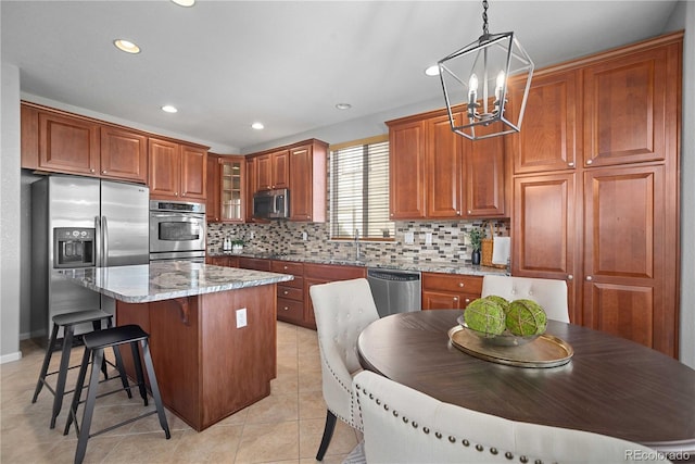 kitchen featuring pendant lighting, appliances with stainless steel finishes, a kitchen island, light stone countertops, and light tile patterned flooring