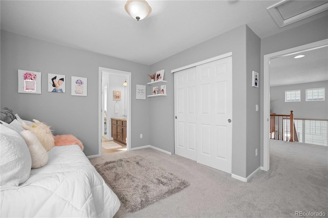 bedroom with ensuite bathroom, light carpet, and a closet