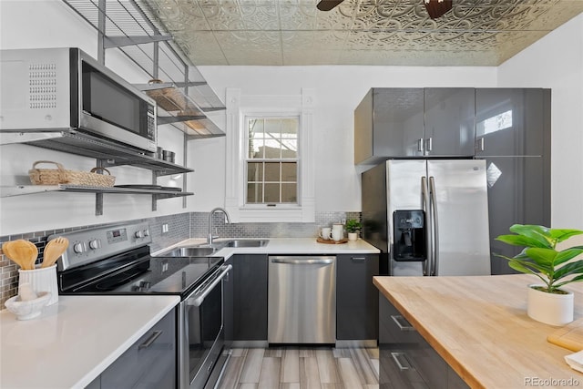 kitchen with sink, light hardwood / wood-style flooring, ceiling fan, backsplash, and stainless steel appliances