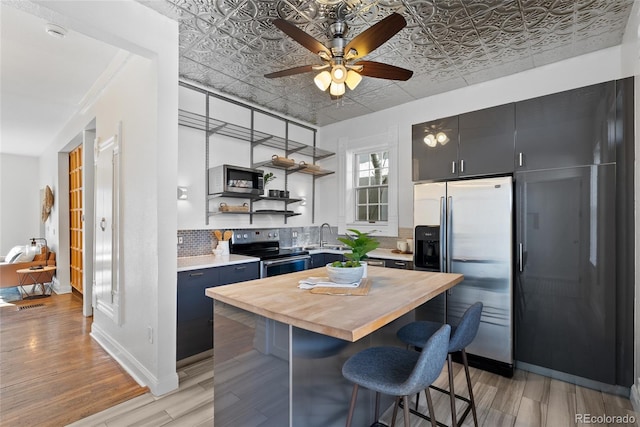 kitchen with appliances with stainless steel finishes, wood counters, backsplash, a kitchen bar, and a center island