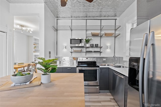 kitchen featuring sink, ceiling fan, stainless steel appliances, decorative backsplash, and light wood-type flooring