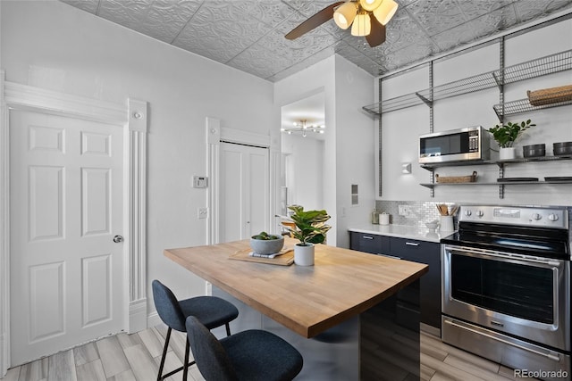 kitchen with a breakfast bar, decorative backsplash, a center island, ceiling fan, and stainless steel appliances