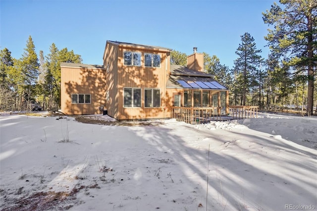 snow covered rear of property with a sunroom