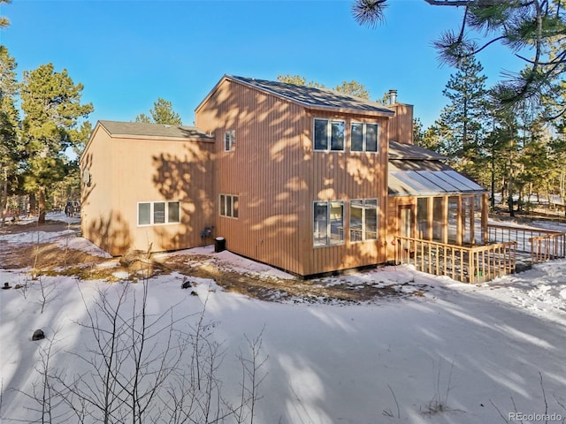 snow covered back of property with a sunroom