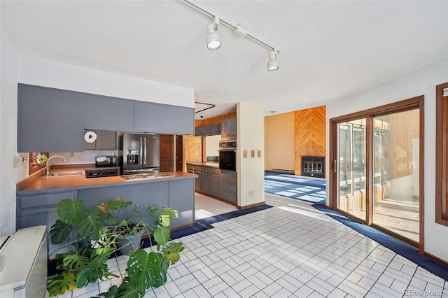 kitchen featuring kitchen peninsula, sink, stainless steel fridge with ice dispenser, gray cabinets, and black oven