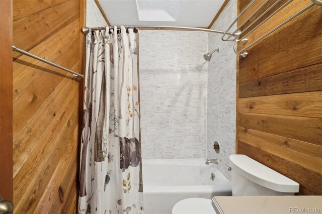 bathroom with wood walls, shower / tub combo, a textured ceiling, and toilet