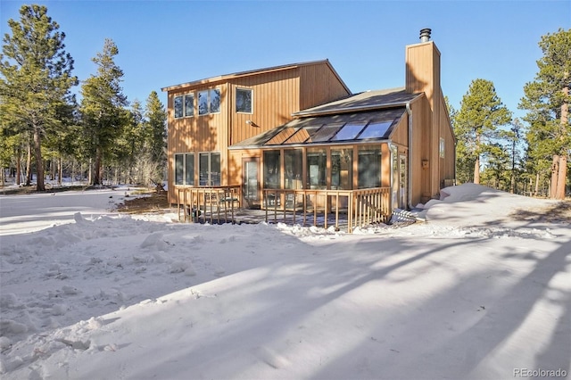 snow covered back of property with a sunroom