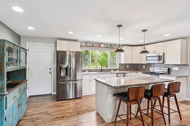 6066 Simms St, Arvada, CO 80004 - kitchen featuring stainless steel appliances, white cabinetry, light stone counters, light wood-type flooring, and recessed lighting