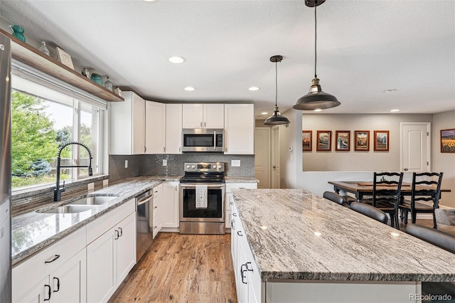 6066 Simms St, Arvada, CO 80004 - kitchen featuring appliances with stainless steel finishes, white cabinets, a center island, decorative backsplash, and recessed lighting