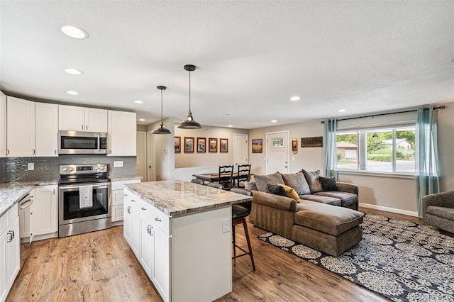 6066 Simms St, Arvada, CO 80004 - kitchen with stainless steel appliances, open floor plan, light wood finished floors, a kitchen island, and recessed lighting