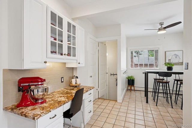 2201 Cherry St, Denver, CO 80207 - kitchen featuring decorative backsplash, white cabinets, a ceiling fan, glass insert cabinets, and light stone countertops