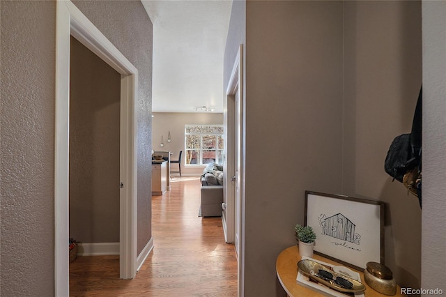 hall featuring light wood-style floors, a textured wall, and baseboards