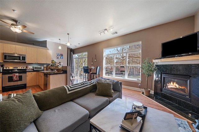 living area with light wood-style flooring, a fireplace, visible vents, and baseboards