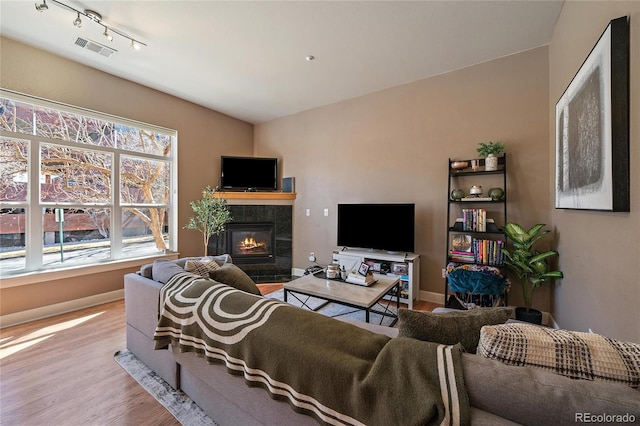 living area featuring a tiled fireplace, wood finished floors, visible vents, and baseboards