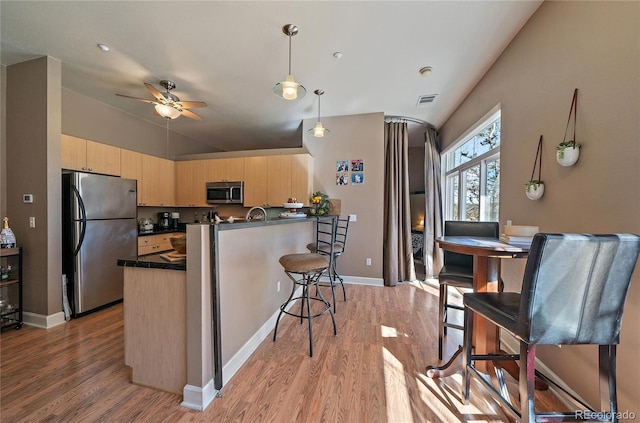 kitchen featuring dark countertops, light wood-style flooring, appliances with stainless steel finishes, light brown cabinets, and a peninsula