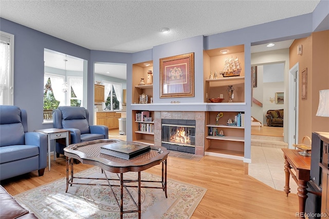 living room with a textured ceiling, a fireplace, light hardwood / wood-style flooring, and built in shelves