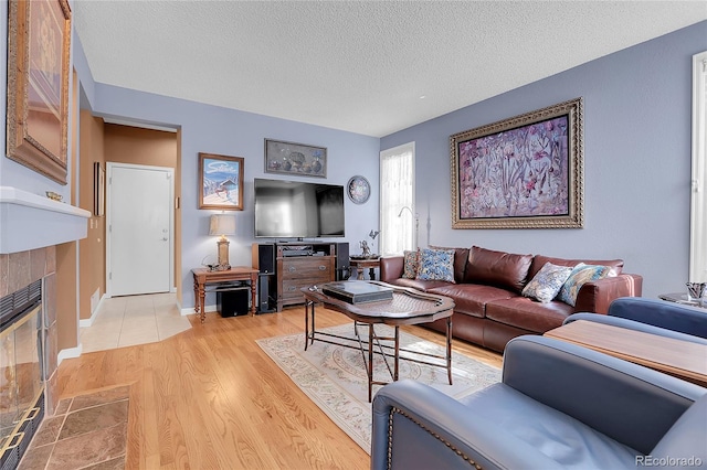 living room with a textured ceiling, a tile fireplace, and light hardwood / wood-style floors