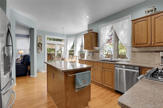 kitchen featuring light hardwood / wood-style floors, stainless steel appliances, a center island, decorative light fixtures, and sink