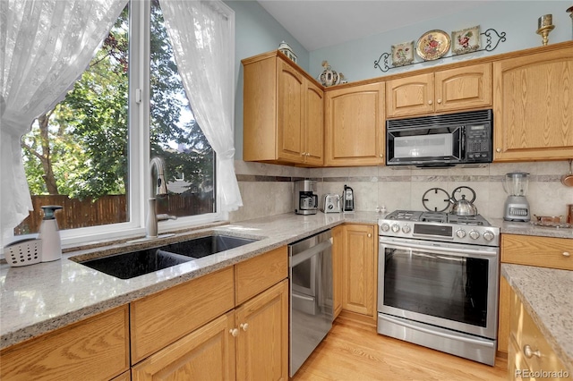 kitchen featuring light stone counters, light hardwood / wood-style floors, sink, decorative backsplash, and stainless steel appliances