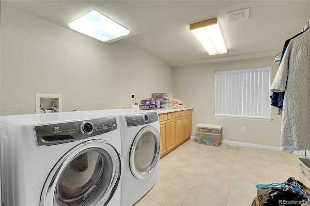 washroom featuring washing machine and clothes dryer, cabinets, and light tile patterned floors