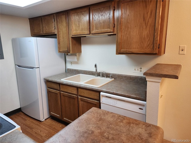 kitchen with dark wood-style floors, white appliances, a sink, and brown cabinets