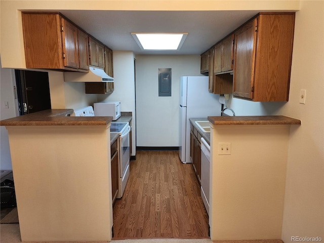 kitchen with white appliances, brown cabinets, a peninsula, under cabinet range hood, and a sink