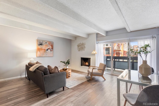 living room featuring a large fireplace, beamed ceiling, a textured ceiling, and wood finished floors